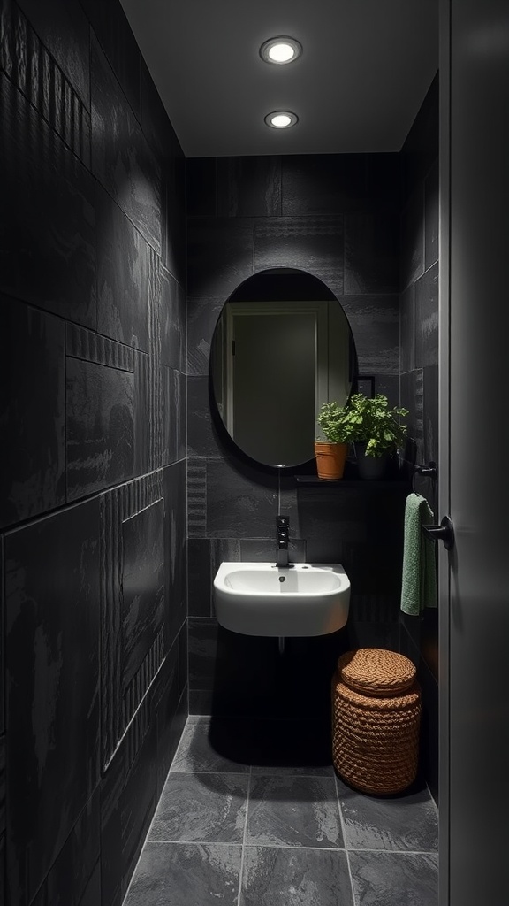 A small dark bathroom featuring textured black wall tiles, a round mirror, a modern sink, a potted plant, and a woven basket.